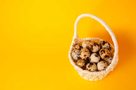 White basket full of quail eggs on bright yellow paper background with copy space, empty place for text. Easter holiday. greeting card. religious mockup design. Health food. farm product.の写真素材