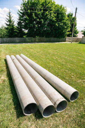 Chrysotile cement pipes lie on the green grass of construction site. Four round tubes. copyspace....