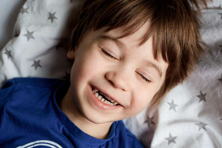 Portrait of beautiful happy 5 year child. Little boy lays on a bed and laughs from tickling. Close...