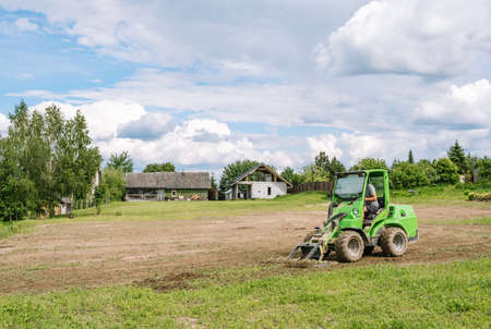 A green mini skid steer loader clear the construction site. Land work by the territory improvement. Small tractor with a ground leveler for moving soil, turf. Machine for agriculture work. copyspace.の写真素材