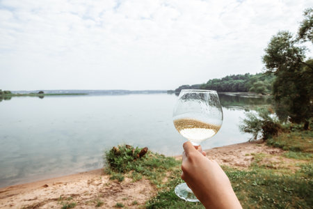 Glass with champagne in woman arm on a nature background. Alcoholic drink with bubbles and foam. summer picnic. Beach bachelorette party concept. Graduation celebration outdoors. copyspace. close-up.の写真素材