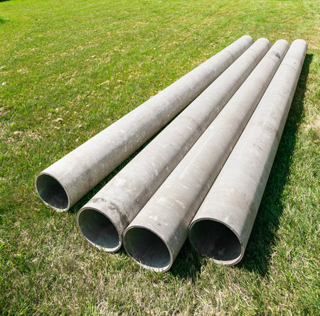 Chrysotile cement pipes lie on the green grass of construction site. Four round tubes. copyspace. building element. column concept. drainage material. Large sewerage culvert. industrial engineering.の写真素材