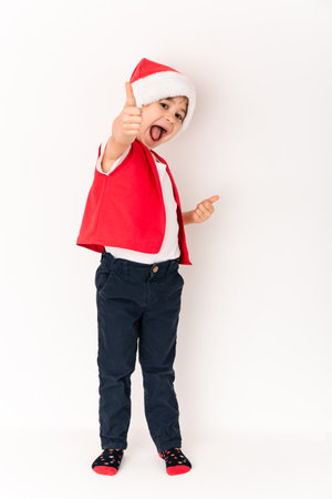 OK sign. Super. Happy handsome caucasian child in a Santa Claus hat isolated on white background with a smile and hands gestures okay. A 5 year old cute European boy in full growth looking at the camera.の写真素材