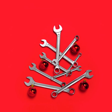Christmas tree made of wrenches decorated with balls on a red background. New Year banner with...