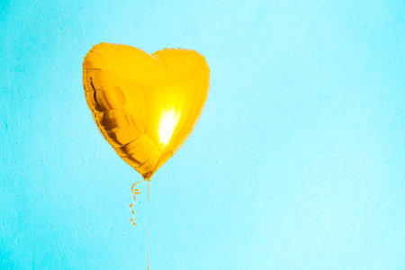 One big yellow heart shaped balloon with ribbon on a blue background with copy space. love symbol. Beautiful birthday party gift. floating objects. Inflatable by helium gas. postcard. Valentine's day.の写真素材