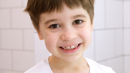 Happy child looks at the camera and smiles. Cute caucasian 6 year old boy in white t-shirt. close-up...