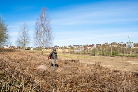 Farmer spraying pesticides and protects the field from weeds and ticks. Man with spray tank equipment. Tillage from ticks and insects. Springtime farm work. dry grass. water jet. manual labor. garden care.の写真素材