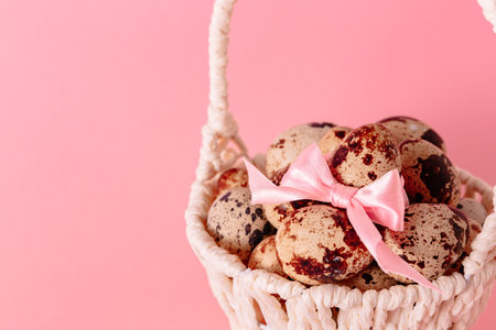 White basket with quail eggs, pink bow and pussy willow on paper background. copyspace. Easter greeting card. religious symbol. Springtime pastel color design. Health food. Empty text place.の写真素材