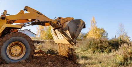 A large yellow wheel loader aligns ground for a new building. Land preparation for the auction or sale. Plot leveling and adding sand for construction. Banner. copyspace. special transport. closeup.の写真素材