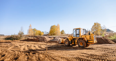 Large yellow wheel loader aligns plot of land for a new building. Land preparation for the auction. Leveling of territory and adding sand for construction site. Banner. copyspace. special transport.の写真素材