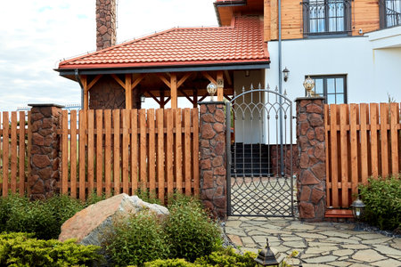 Entrance group of private house with wooden fence, pillars finished with decorative stone, lights, forged gate. Landscaping. Large stone. green planting. Territory achievement. natural materials.の写真素材