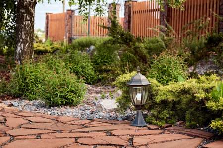 Entrance group of private house with wooden fence, stone pillars, lights, forged gate, paved path with red natural stone and flowerbed. Landscaping. boulders. Green planting territory accomplishment.の写真素材