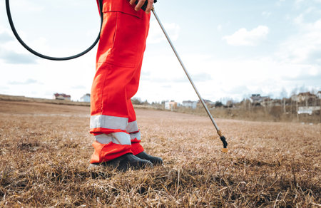 Farmer spraying pesticide on lawn field wearing protective clothing. Treatment of grass from weeds and dandelion. pest control. Insecticide sprayer with a proper protection. gardening care season.の写真素材