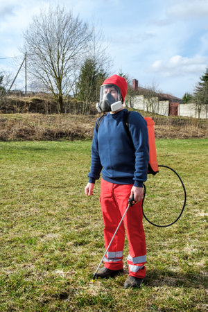 Man gardener wearing protective clothing and full face respirator mask with dust filters and backpack, knapsack, shoulder-mounted battery sprayer. PPE. safety precautions. Equipment for pest control.の写真素材