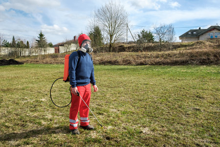 Man gardener wearing protective clothing and full face respirator mask with dust filters and backpack, knapsack, shoulder-mounted battery sprayer. PPE. safety precautions. Equipment for pest control.の写真素材