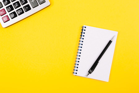 Large silver calculator with black pen and white paper notebook on a yellow background. Conceptual photo of calculations, accounting, computing, profit, loss, tax with place for text. business bannerの写真素材