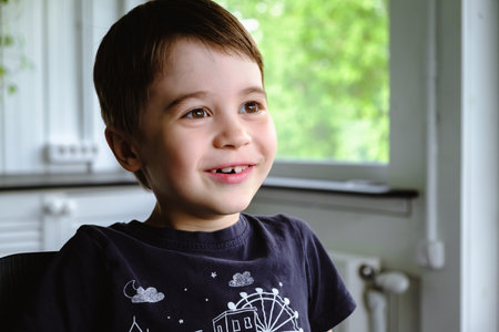 Happy 6 year old boy child is smiling enjoying life. Concept of happy childhood. Portrait of young boy sitting in home background, indoors. adorable face. Nice smile with beautiful teeth. side view.の写真素材
