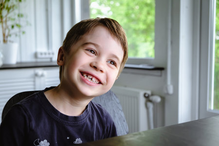 Happy 6 year old boy child is smiling enjoying life. Concept of happy childhood. Portrait of young boy sitting in home background, indoors. adorable face. Nice smile with beautiful teeth. side view.の写真素材