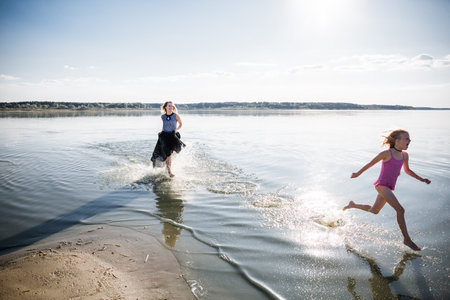 Mother and daughter have fun running in water with splashing. The state of happiness, freedom and independence. Strengthening parent-child relationships, physical and psychological health in the family.の写真素材
