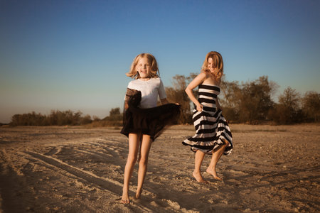 Mother and daughter in dresses jumping and dancing on the beach at sunset. Good relations between generations. have fun. family pastime. Health promotion by outdoor activities. vacation. Sisterhood.の写真素材