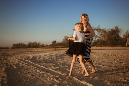 Mother and daughter in dresses jumping and dancing on the beach at sunset. Good relations between generations. have fun. family pastime. Health promotion by outdoor activities. vacation. Sisterhood.の写真素材