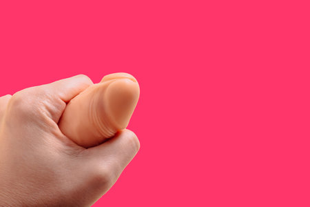 Sex toy in hand. Big latex dildo. BDSM strapon with leather on pink background with copy space....