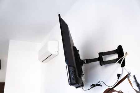Flat screen TV hanging on a metal mount on the white wall in the room. Black TV bracket, mount bracket for LCD monitor, plasma TV and LED display device. Copy space. Side view.の写真素材