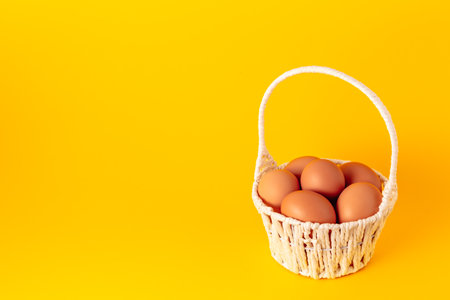 Eggs in straw basket on yellow background. Easter holiday card. Copy space. Empty text place. Springtime mockup design. Healthy food. Farm production. Close-up. Business card.の写真素材
