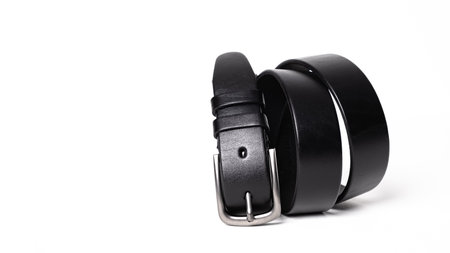 Twisted black leather belt with matted metal buckle isolated on white background. Fastened fashionable unisex, man or woman accessory for trousers, jeans, dress. Male luxury strap. Haberdashery goods.の写真素材