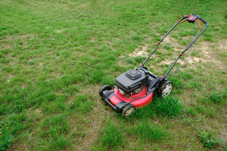 Lawn mover on green grass background. Machine for cutting lawns. Garden care. Electric equipment. Side view. Copy space. Lots of clover weeds. Sport lawn field for games. Banner. High quality photo.の写真素材