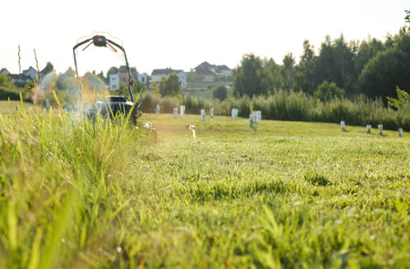 Lawn mower on green grass background in the garden. Low angle of view. Machine for cutting lawns. Cutting of meadow plants. Summer gardening. Banner with copy space.の写真素材