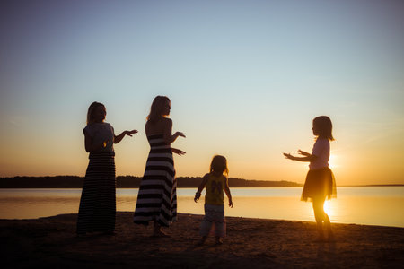 Silhouette of groupe dancing people at sunset. Childhood and motherhood happiness concept. Women and children. Summertime season. Joyful emotions. Summer vacation. Holidays. Birthday mood. Seascape.の写真素材
