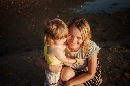 Smiling mom hugs her little 2 year old daughter on the sunset on the beach. Happy family parent-child relationship. Love and happiness concept. Trust and acceptance. Psychological comfort. Summer.の写真素材
