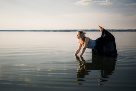 A beautiful young woman in a dress stands on all fours in the water in a sexy pose. Copy space. Fashion concept. Energy of water, earth and sun. Dedication. Witch ritual. State of pleasure and bliss.の写真素材