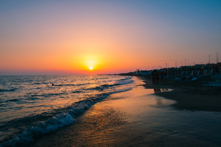 Sunset on the Mediterranean Sea. Calm waves and bright low sun. Side view of the water and beach. The concept of an evening walk on vacation. Coastline. Holidays in Italy. Nature wallpaper.の写真素材