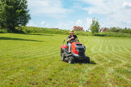 Man on lawn tractor mowing lawn on backyard. The red rider. The lawnmower tractor. High quality 4k footage.の写真素材