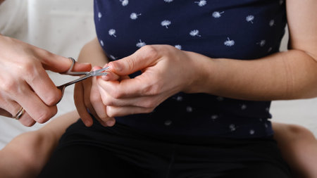 Childrens manicure. Mother is cutting nail on hand to her child with scissors. Body care concept. Carefully hygiene. Healthy lifestyle. Close-up body part. Mom takes care of the baby.の写真素材