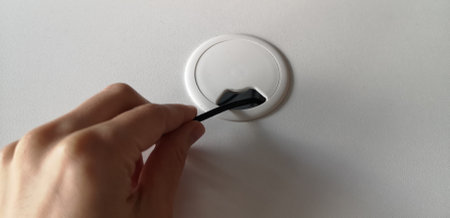 Hole for electric wire and cable on computer desk. Person holds the black wire. Comfortable furniture on the table. White color. Top view. High quality photo.の写真素材