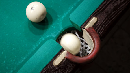 Playing Russian billiards on a green table. A white ball rolls and hits another which pockets into...