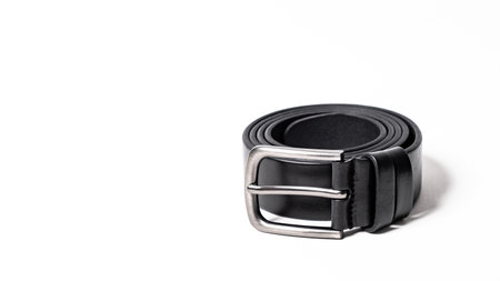Twisted black leather belt with matted metal buckle isolated on white background. Fastened fashionable unisex, man or woman accessory for trousers, jeans, dress. Male luxury strap. Haberdashery goods.の写真素材
