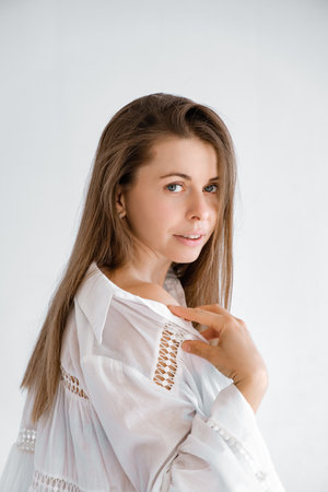Pretty 30s woman looking at camera in white top shirt showing her shoulder. Studio portrait. Boho style dress. Natural beauty face. Concept of tenderness and femininity. Flirting look.の写真素材