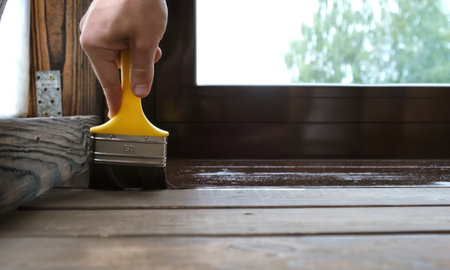 Close-up of a brush painting wood floor in brown color. Wood plank impregnation. Finish oil coating of board. Second layer of oiling. Manual construction work in a gazebo. Natural building materials.の写真素材