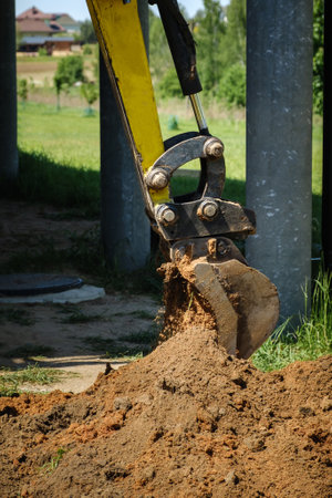 Mini excavator digs a narrow trench in soil for laying communications close-up. Mini bucket of...
