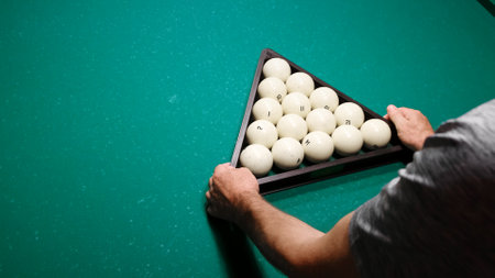 The player places the triangle with billiard balls in the designated place on the green pool table. Preparing the pyramid for the new game. Pastime playing sport hobby. Copy space.の写真素材