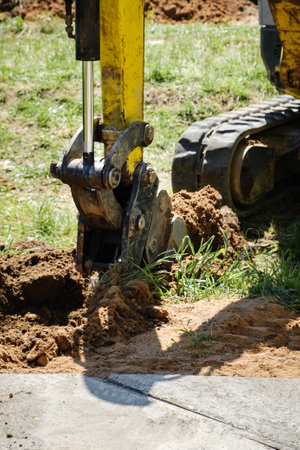 Mini excavator digs a narrow trench in soil for laying communications close-up. Mini bucket of...