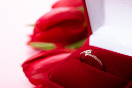 Diamond ring in box lais on a big bouquet of red tulips on pink background. Symbol of love. Jewelry...