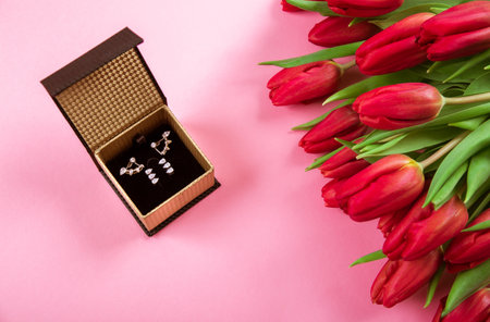 Diamond ring in box lais on a big bouquet of red tulips on pink background. Symbol of love. Jewelry gift certificate. Holiday business card. Engagement concept. Copy space. Top view.の写真素材
