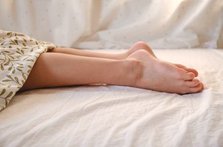 The child's bare feet sticking out from under the blanket. The kid sleeping on the stomach. Relax in...