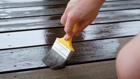 Close-up of a brush painting wood floor in brown color. Wood plank impregnation. Finish oil coating of board. Second layer of oiling. Manual construction work in a gazebo. Naturalの写真素材