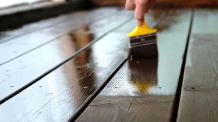 Close-up of a brush painting wood floor in brown color. Wood plank impregnation. Finish oil coating of board. Second layer of oiling. Manual construction work in a gazebo. Naturalの写真素材